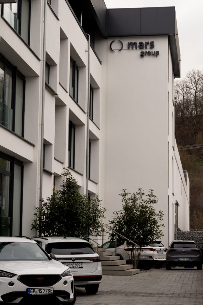 Außenansicht des modernen Mars Group Gebäudes in Göppingen mit Firmenlogo an der Fassade und geparkten Autos im Vordergrund.