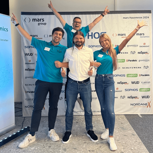 Mars Solutions CEO (mittig) steht mit Partnern – darunter Herr Niedling (links) und eine Kollegin (rechts) – vor der gebrandeten Sophos-Fotowand, die Hände jubelnd in die Luft gereckt.