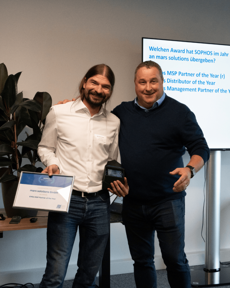 Zwei Männer stehen zusammen, einer hält eine Auszeichnung und der andere eine Trophäe in einem modernen Raum.