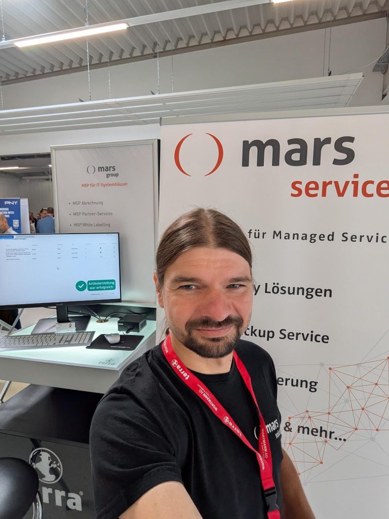 Geschäftsführer von mars solutions GmbH steht am Messestand mit einem Bildschirm im Hintergrund.