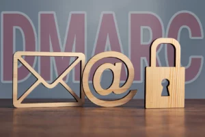 Holzbuchstaben und Symbole, die ein E-Mail-Symbol, ein @-Symbol und ein Vorhängeschloss darstellen und im Hintergrund liegt ein DMARC Schriftzug.